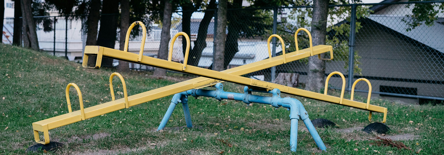 Playground seesaw with yellow beams and blue supports on a grassy area.